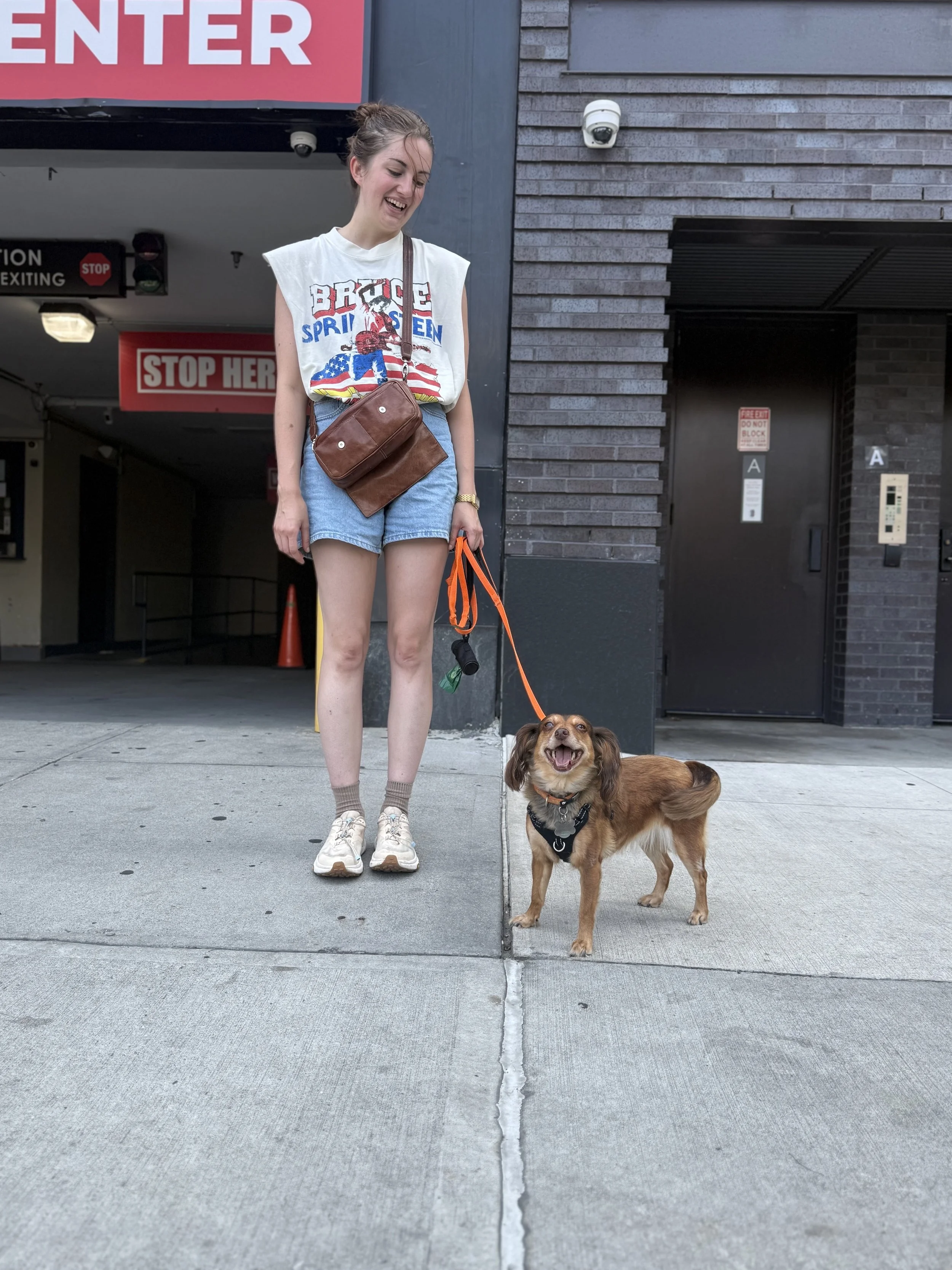 Client Kelly smiling with her small brown dog Rosie on an orange leash in Brooklyn